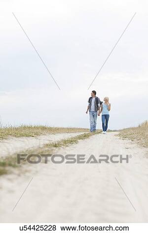 Stock Photo - Full length of young hiking couple walking on path at field. Fotosearch