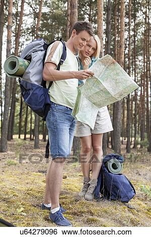 Stock Photograph - Full length of young hiking couple reading map in forest. Fotosearch
