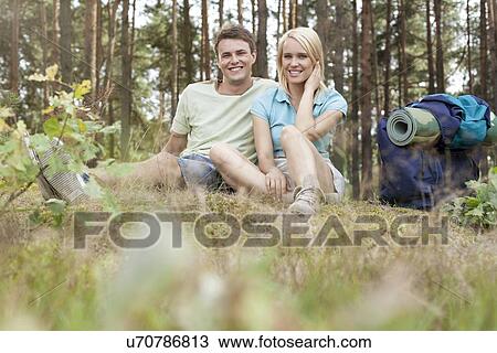 Stock Image - Full length of young hiking couple with backpack relaxing in forest. Fotosearch