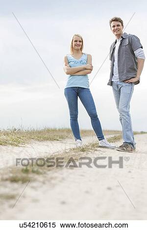 Full length portrait of young couple standing on trail at field View Large Photo Image Stock Photography - Full length portrait of young couple standing on trail at field. Fotosearch