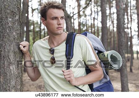 Stock Photo - Handsome young man with backpack hiking in forest. Fotosearch