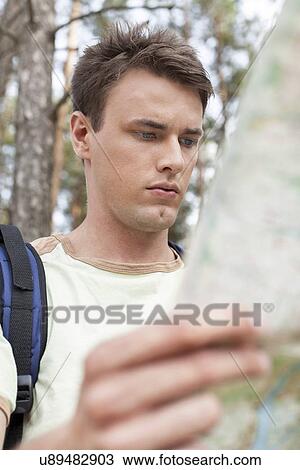 Stock Image - Handsome young man with backpack reading map in forest. Fotosearch