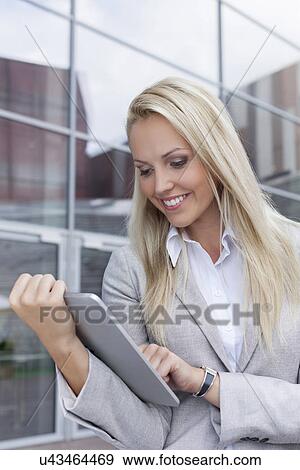 Stock Photo - Happy beautiful businesswoman using digital tablet against office building. Fotosearch
