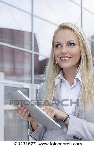 Happy businesswoman using digital tablet while looking away against office building View Large Photo Image Stock Photo - Happy businesswoman using digital tablet while looking away against office building. Fotosearch