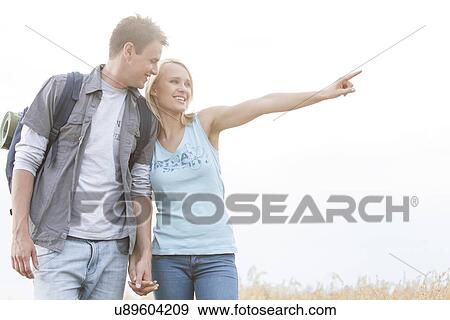 Stock Photo - Happy female hiker showing something to man on field against clear sky. Fotosearch