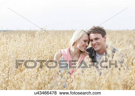 Happy loving young couple sitting amidst field View Large Photo Image Stock Photo - Happy loving young couple sitting amidst field. Fotosearch