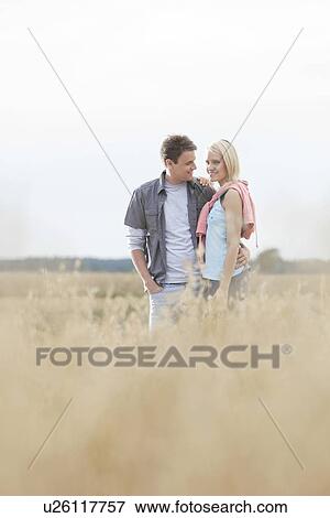 Happy loving young couple standing together at field View Large Photo Image Stock Photo - Happy loving young couple standing together at field. Fotosearch
