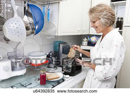 Stock Photography - Happy senior woman preparing toast in domestic kitchen. Fotosearch