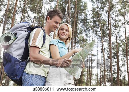 Stock Image - Happy young backpackers reading map in woods. Fotosearch