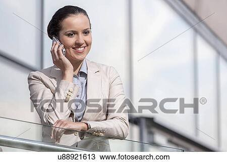 Happy young businesswoman using cell phone at office railing View Large Photo Image Stock Image - Happy young businesswoman using cell phone at office railing. Fotosearch