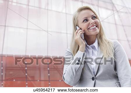 Happy young businesswoman using cell phone against office building View Large Photo Image Stock Photo - Happy young businesswoman using cell phone against office building. Fotosearch