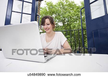 Stock Image - Happy young businesswoman using laptop at desk. Fotosearch