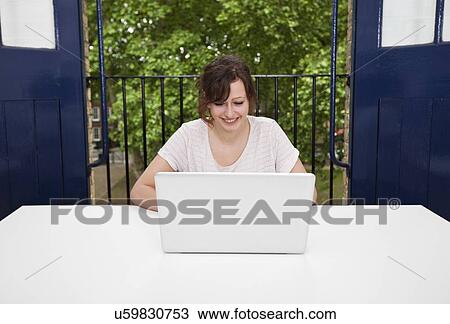 Stock Image - Happy young businesswoman using laptop at desk. Fotosearch