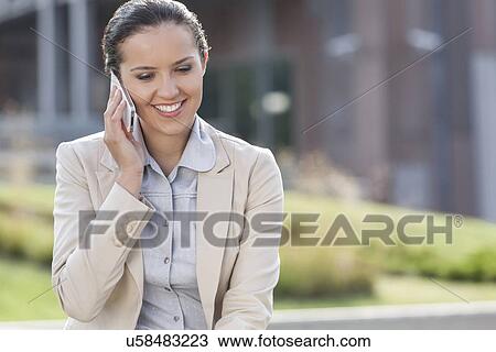 Stock Image - Happy young businesswoman using mobile phone while looking down outdoors. Fotosearch