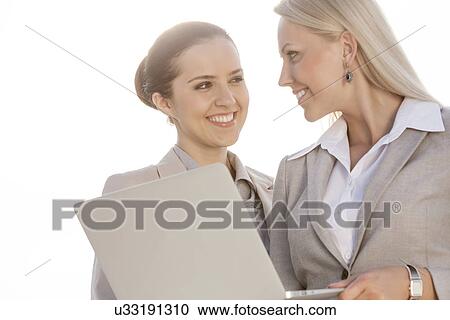 Happy young businesswomen with laptop looking at each other against sky View Large Photo Image Stock Image - Happy young businesswomen with laptop looking at each other against sky. Fotosearch