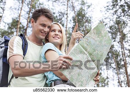 Happy young hiking couple holding map with woman pointing away in forest View Large Photo Image Stock Image - Happy young hiking couple holding map with woman pointing away in forest. Fotosearch