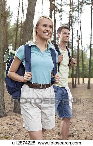 Stock Photography - Happy young woman with man trekking in forest. Fotosearch