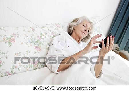 High angle view of senior woman using smart phone in bed at home View Large Photo Image Stock Photograph - High angle view of senior woman using smart phone in bed at home. Fotosearch