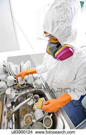 Picture - High angle view of woman in gas mask washing utensil at kitchen sink. Fotosearch