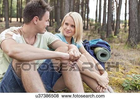Hiking couple looking at each other while relaxing in forest View Large Photo Image Stock Photo - Hiking couple looking at each other while relaxing in forest. Fotosearch