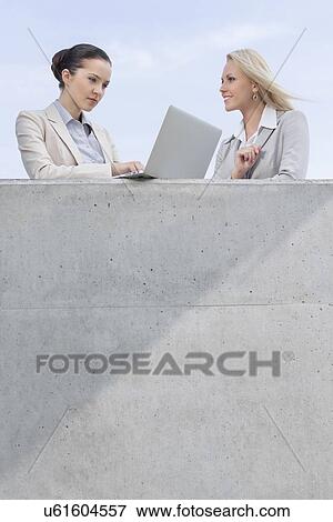 Low angle view of businesswoman using laptop while standing with coworker on terrace against sky View Large Photo Image Stock Photo - Low angle view of businesswoman using laptop while standing with coworker on terrace against sky. Fotosearch