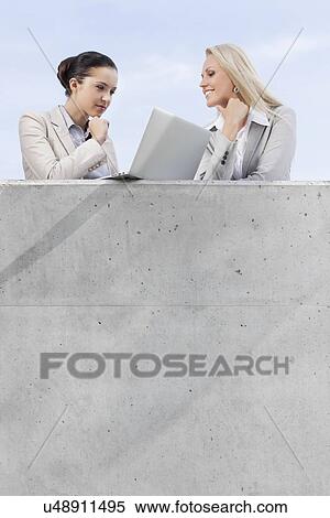 Low angle view of businesswomen looking at laptop while standing on terrace against sky View Large Photo Image Stock Photography - Low angle view of businesswomen looking at laptop while standing on terrace against sky. Fotosearch