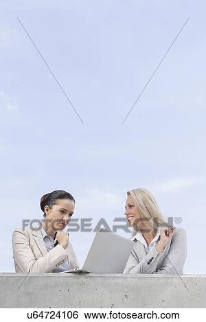 Low angle view of concentrated businesswoman using laptop while standing with coworker on terrace against sky View Large Photo Image Stock Photograph - Low angle view of concentrated businesswoman using laptop while standing with coworker on terrace against sky. Fotosearch