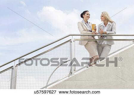Low angle view of happy businesswomen discussing while standing by railing against sky View Large Photo Image Stock Photo - Low angle view of happy businesswomen discussing while standing by railing against sky. Fotosearch