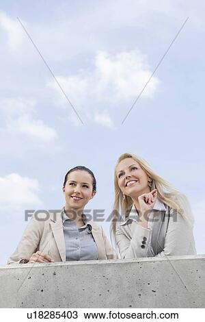 Low angle view of happy young businesswomen looking away while standing on terrace against sky View Large Photo Image Stock Image - Low angle view of happy young businesswomen looking away while standing on terrace against sky. Fotosearch