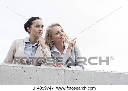 Low angle view of happy young businesswoman showing something to colleague while standing on terrace against sky View Large Photo Image Stock Photo - Low angle view of happy young businesswoman showing something to colleague while standing on terrace against sky. Fotosearch