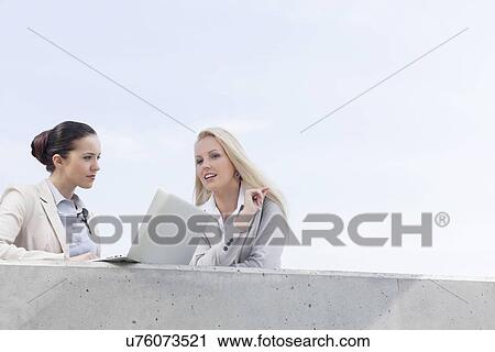 Low angle view of young businesswomen with laptop discussing while standing on terrace against sky View Large Photo Image Stock Image - Low angle view of young businesswomen with laptop discussing while standing on terrace against sky. Fotosearch