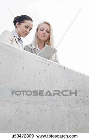 Low angle view of young businesswomen using digital tablet together while standing on terrace against sky View Large Photo Image Stock Photo - Low angle view of young businesswomen using digital tablet together while standing on terrace against sky. Fotosearch