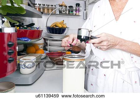 Stock Photo - Midsection of senior woman filling ground espresso in portafilter at kitchen counter. Fotosearch