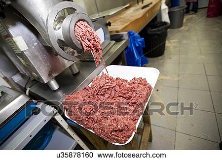 Stock Image - Minced meat falling from machine in container at store. Fotosearch