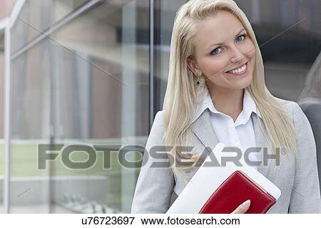 Stock Photo - Portrait of beautiful businesswoman with organizer and digital tablet by glass wall. Fotosearch