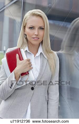 Portrait of beautiful businesswoman holding organizer and digital tablet while leaning on glass wall View Large Photo Image Stock Photograph - Portrait of beautiful businesswoman holding organizer and digital tablet while leaning on glass wall. Fotosearch