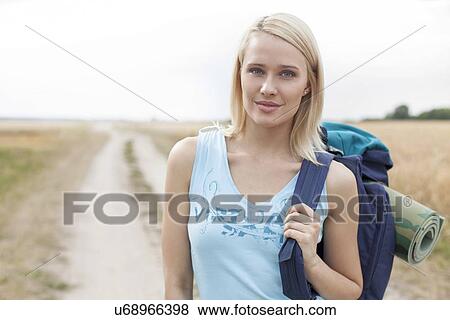 Stock Photo - Portrait of beautiful female hiker with backpack standing on field. Fotosearch