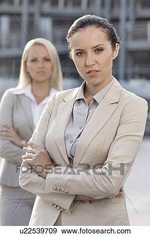 Stock Photo - Portrait of confident young businesswoman with female colleague in background. Fotosearch