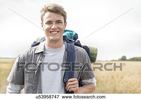 Stock Photo - Portrait of handsome male hiker with backpack standing on field. Fotosearch
