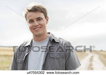 Stock Image - Portrait of handsome young man standing on field. Fotosearch