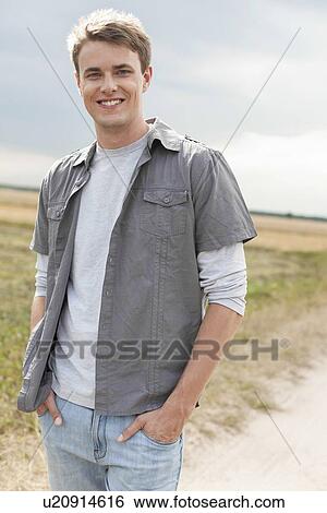 Portrait of handsome young man with hands in pockets standing on field View Large Photo Image Stock Photograph - Portrait of handsome young man with hands in pockets standing on field. Fotosearch