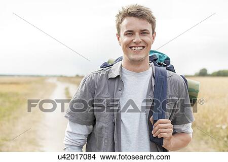 Picture - Portrait of happy male hiker with backpack standing on field. Fotosearch
