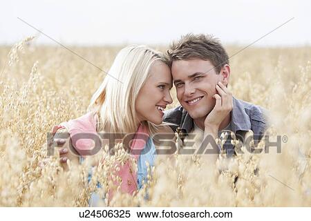 Portrait of happy man sitting with romantic woman amidst field View Large Photo Image Stock Photography - Portrait of happy man sitting with romantic woman amidst field. Fotosearch