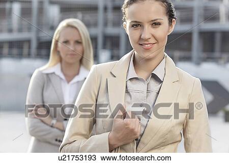 Portrait of happy young businesswoman with female colleague in background View Large Photo Image Stock Image - Portrait of happy young businesswoman with female colleague in background. Fotosearch