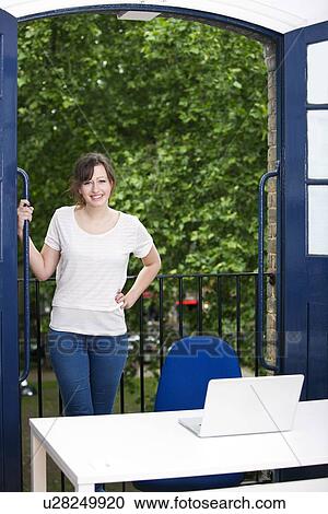Portrait of happy young businesswoman standing by balcony with laptop on desk View Large Photo Image Stock Image - Portrait of happy young businesswoman standing by balcony with laptop on desk. Fotosearch
