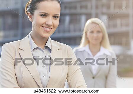 Portrait of happy young businesswoman with female colleague in background View Large Photo Image Stock Image - Portrait of happy young businesswoman with female colleague in background. Fotosearch