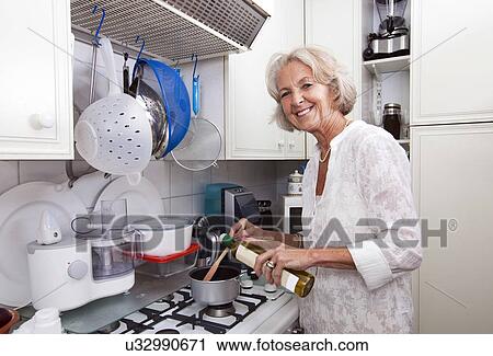 Portrait of senior woman adding olive oil to saucepan at kitchen counter View Large Photo Image Stock Image - Portrait of senior woman adding olive oil to saucepan at kitchen counter. Fotosearch