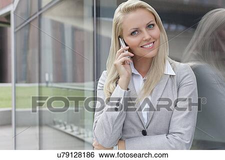 Portrait of young businesswoman communicating on cell phone while leaning on glass wall View Large Photo Image Stock Photograph - Portrait of young businesswoman communicating on cell phone while leaning on glass wall. Fotosearch