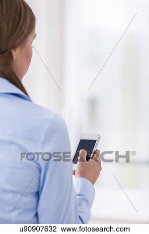 Stock Image - Rear View of a Woman holding a smart phone. Fotosearch