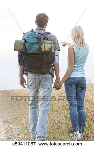 Rear view of female hiker showing something to man on field View Large Photo Image Stock Photo - Rear view of female hiker showing something to man on field. Fotosearch